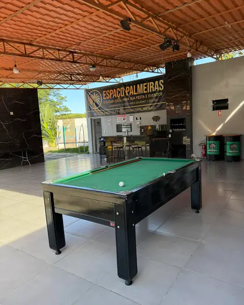 Salão coberto com mesa de sinuca em primeiro plano e, ao fundo, a área gourmet com churrasqueira e o banner do Espaço Palmeiras.