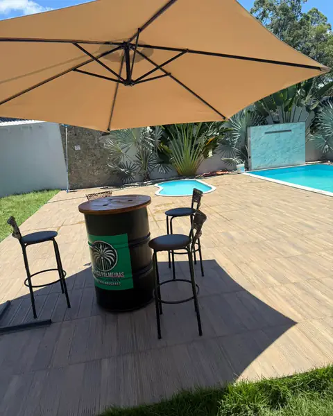 Mesa bistrô com banquetas sob ombrelone, no deck ao lado das piscinas.